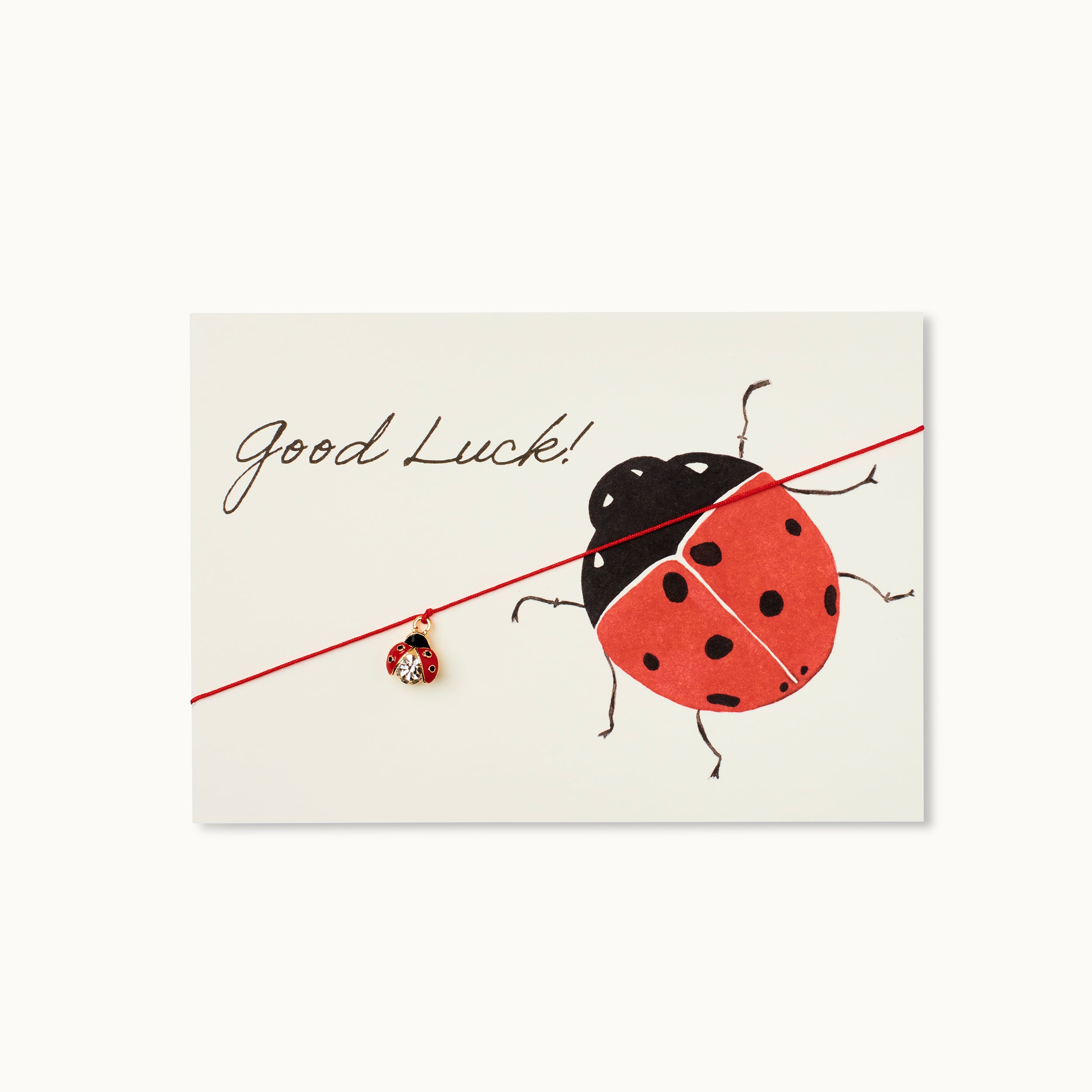 Good Luck! Karte mit einem Marienkäfer als 18K vergoldeter Anhänger an einem roten Armband.