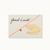 Good Luck! Karte mit einem Glückskeks als 18K vergoldeter Anhänger an einem neonorangenen Armband. 